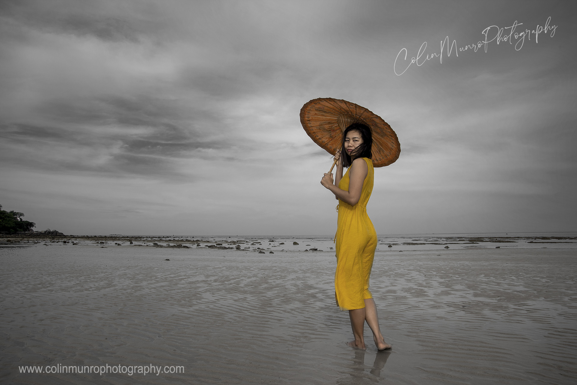 A Thai lady in a bright yellow dress walks along a beach in Thailand.