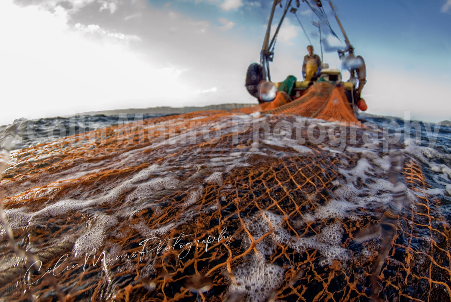 A trawl net, full of fish, as it is hauled to the surface. Picture taken from directly above the net, at sea level, looking towards the stern of the boat. ©Colin Munro Photography